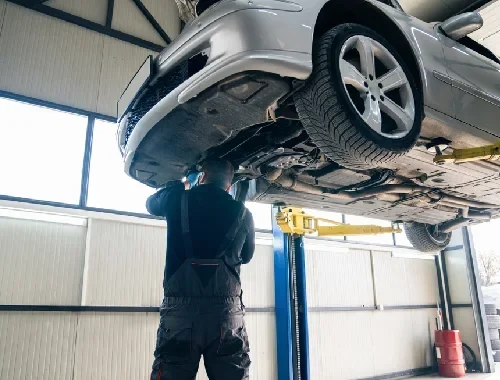 Mechanic inspecting suspension and steering parts under a vehicle